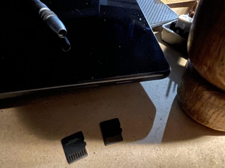 Close-up images of a couple flash cards sitting in front of a laptop and a tablet. On the tablet is a screwdriver handle and to the right is the head of a gavel casting a shadow over the assemblage of items.