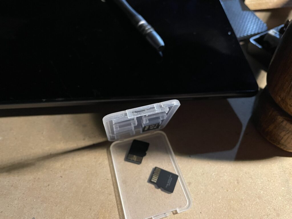 A close up photograph of flash cards in a case next to a laptop, tablet with a screwdriver handle on top. To the right is a gavel that is casting a shadow on the assortment of items.